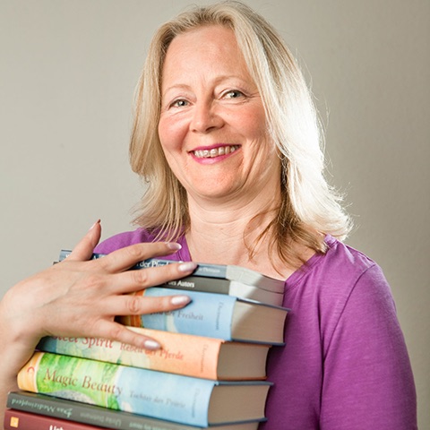 Ulrike Dietmann, die Gründerin der Pegasus Schreibschule, hält stolz eine Sammlung ihrer eigenen veröffentlichten Bücher in den Händen. Tauche ein in ihre Welt des Schreibens und entdecke die inspirierende Kraft der Worte.